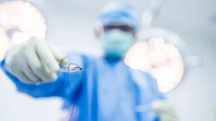 Fotobehang Selective focus on surgical needle holder with blur background.Surgeon or doctor inside operating room did suture while surgery in hospital.Orthopedic or cosmetic and surgical emergency surgery. © Issara