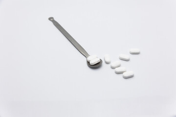 Painkillers on a white refined silver medicine spoon on a white background
