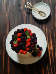 Selective focus of Decorated by strawberries raspberries white naked cake, rustic style for weddings, birthdays and events. On brown background. Selective focus. In kitchen