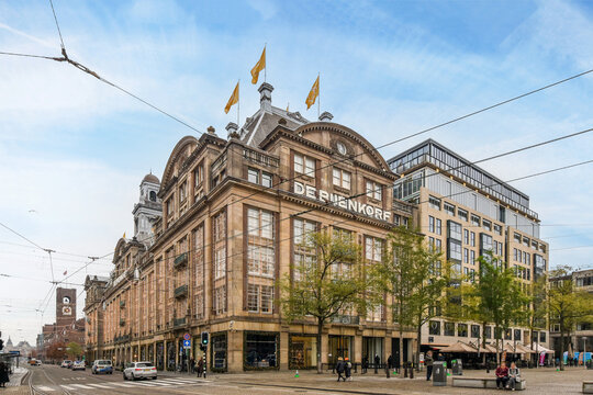 Amsterdam, Netherlands - 10 April, 2021: An Old Building On The Corner Of A City Street With People Walking Around It And Cars Driving Down The Road