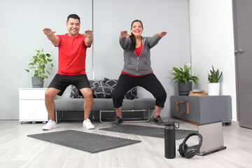 Latino adult couple of man and woman exercise at home taking online class they see the laptop in...