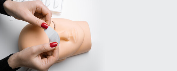 Training eyelash extensions. Hands of cosmetologist are preparing the strip under eyes of on a mannequin before the eyelash extension procedure. Banner.