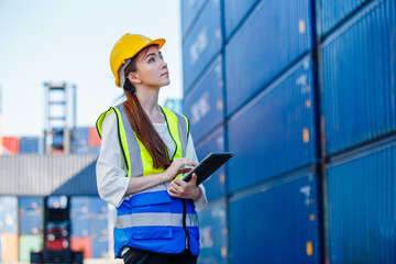 Female industrial engineer in uniform wearing safety hard hat using tablet checking containers...