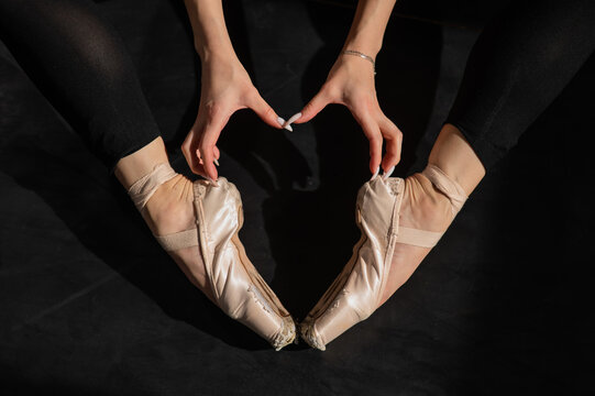A faceless ballerina sits on the floor and makes a heart shape with her hands and pointe shoes. Top view. 
