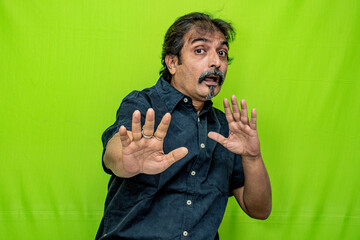 The well-dressed Indian man, wearing a black shirt, suddenly flailed his hands and contorted his face in a terrified expression while standing against a green screen background