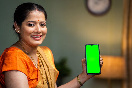 happy smiling woman showing green screen mobile phone by looking at camera on chair - concept app or application promotion, advertisement and internet