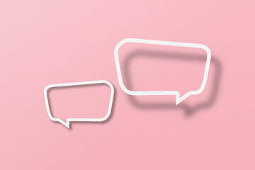 White paper cut out speech bubble shape set on pink paper background.