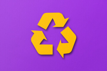 Yellow paper cut into recycled shape isolated on purple paper background.