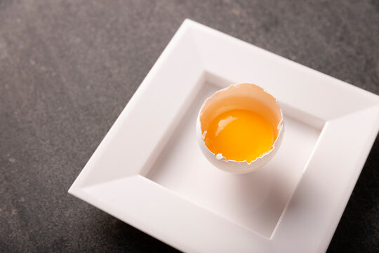 Half broken egg with yolk on stone table. Very popular nutritious and economic food product. Closeup image.