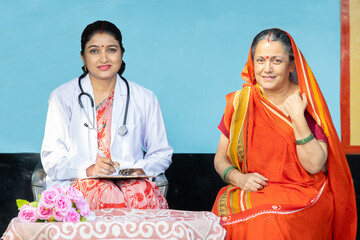 Rural healthcare camp concept. Young indian female doctor and senior woman patient sitting together...