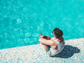 Handsome man sitting near the swimming pool of a cruise ship. Sunny morning, clear day. View from...