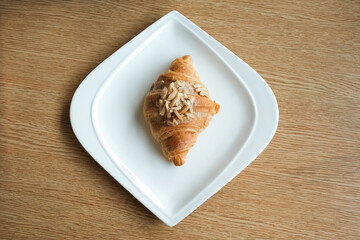 Fresh almond croissant on white plate on a wooden table.