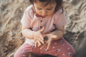 Adorable toddler girl playing on the sand holding in hand some stones that they examine carefully. Small child enjoying vacation. Travelling with kids