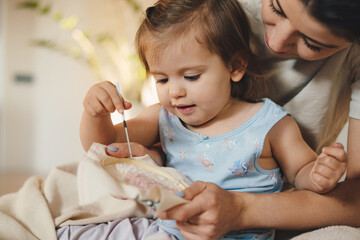 Woman teaching her baby daughter embroidering at home, close-up view. For lifestyle design. Family...