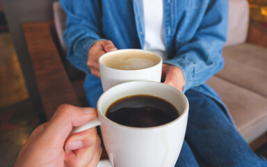 Closeup image of a couple people clinking white coffee mugs in cafe