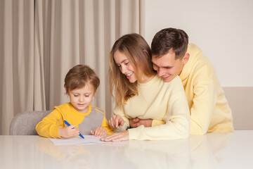 Fototapeta premium Adorable family, cute parents in yellow clothes with their child son drawing