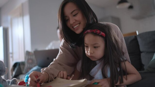 Smiling Asian young girl painting with her mother at home