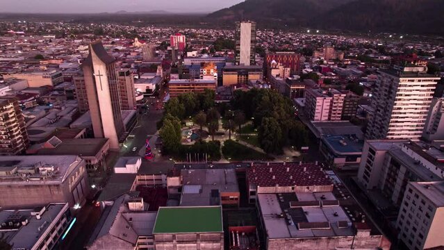 Aerial orbit of the Plaza de Armas Anibal Pinto and the Cathedral Church of Temuco in the blue hour with purple colors and the street illuminated at night, Temuco, Chile.