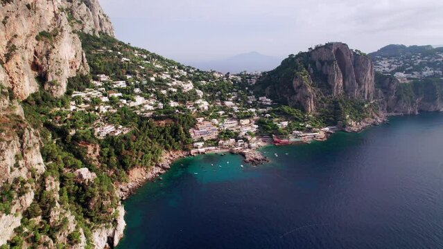 A wide aerial shot of the beautiful beaches and rocky cliff landscape around Marina Piccola on Capri, a famous island that is a popular luxury vacation destination in Italy along the Amalfi Coast.