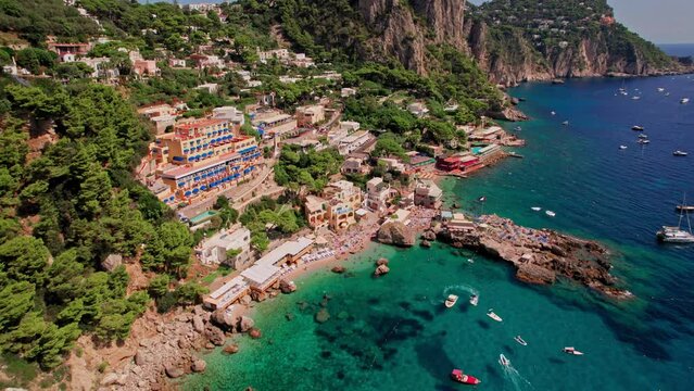 A cinematic aerial shot of the beautiful cliffs and beach landscape of Marina Piccola on the island of Capri, a popular tourist destination along the Amalfi Coast in the Bay of Naples in Italy.