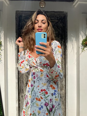 Woman in summer dress with flower spring print at home outdoor take photo selfie on phone in mirror...