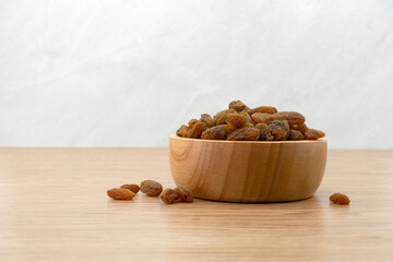 Raisins in wooden bowl on wooden texture background. Dry raisins. Bulk raisins grains.