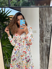 Woman in summer dress with flower spring print at home outdoor take photo selfie on phone in mirror for social media, stories, vertical