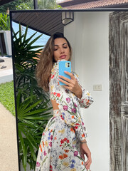 Woman in summer dress with flower spring print at home outdoor take photo selfie on phone in mirror...