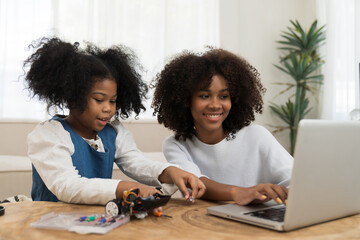 Young female teacher and child girl learning toy robotics technology with laptop computer at home. Two student building robotic toy car in classroom at school. Education and technology concept
