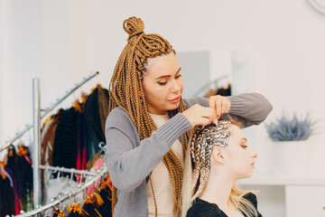 Hairstylist braided afro braids dreadlocks kanekalon pigtails hair of female client in barber salon.