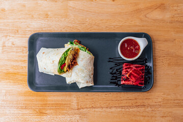 wrap mexican food on a black rectangular plate on a wooden table