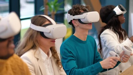 Business conference in VR in an office. Multiracial group of people. A young man teaching others how to use VR glasses and controllers, papers and gadgets on the table