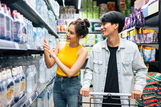 Asian young man and woman using cart to shoping goods in supermarket. 