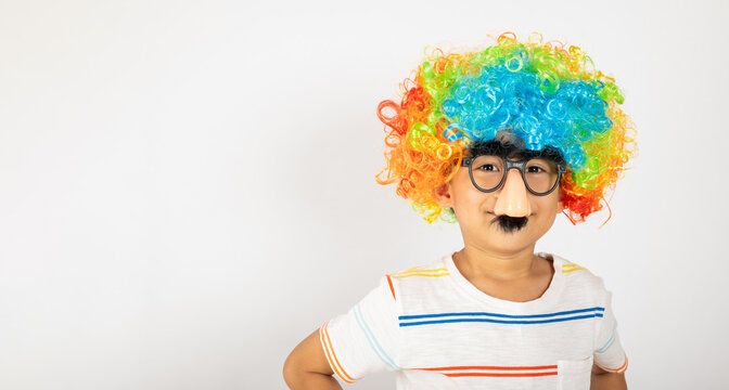 April Fool's Day. Portrait of Funny kid boy clown wears a curly wig colorful a big nos and glasses and has a mustache isolated on white background with copy space, Happy child festive decor
