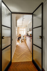 Woman sits by the dining table with her dog in the kitchen of bright and stylish apartment, view through the opened glass door