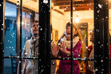 Adorable child looking at the window and first snow flakes with family. 