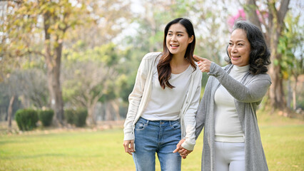 Happy Asian grandmother enjoys talking with her lovely grandchild while strolling in the park
