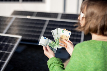 Woman counts euro banknotes saved due to the generation of energy from a solar power plant...