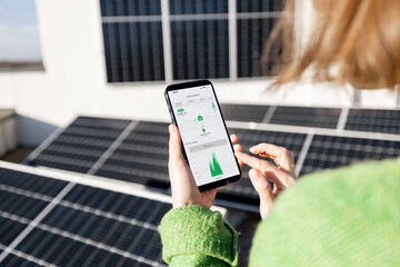 Woman monitors energy production from the solar power plant with mobile phone. Close-up view on phone screen with running program. Concept of remote control of solar energy production - obrazy, fototapety, plakaty