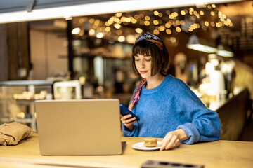 Young stylish woman works on laptop while sitting with a coffee drink at modern cafe. Concept of...
