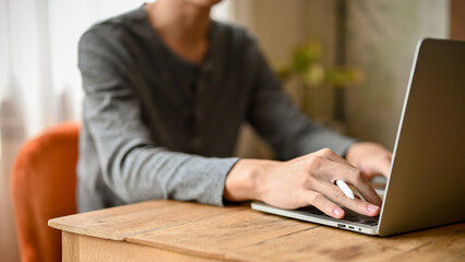 Close-up and cropped image of an Asian man in casual clothes typing on keyboard, using laptop