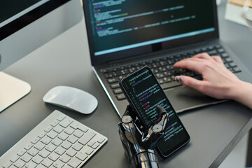 Close-up of developer typing security codes on smartphone and laptop for new computer program