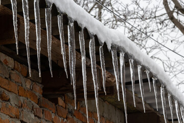 Sharp icicles and melted snow hanging from eaves of roof. Beautiful transparent icicles slowly gliding of a roof