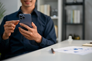 Cropped image of happy Asian businessman using his phone at his desk in the office.