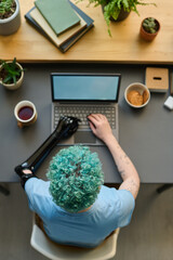 High angle view of young girl with prosthetic arm typing on laptop sitting at her workplace