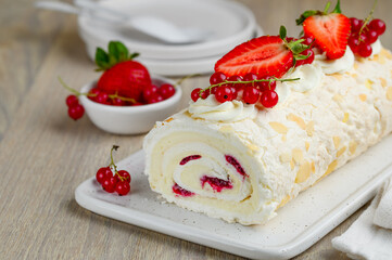 A piece of meringue roll with cream and berry confiture decorated with fresh strawberries and red currants. Close up. Selective focus.