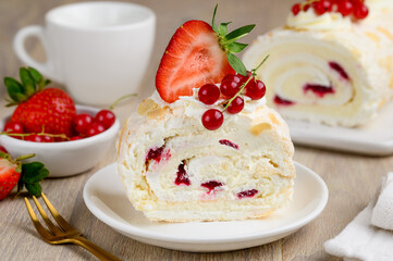 A piece of meringue roll with cream and berry confiture decorated with fresh strawberries and red currants. Close up. Selective focus.