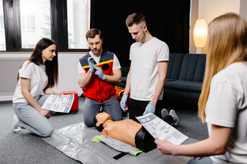 Young man instructor helping to make first aid heart compressions with dummy during the group...