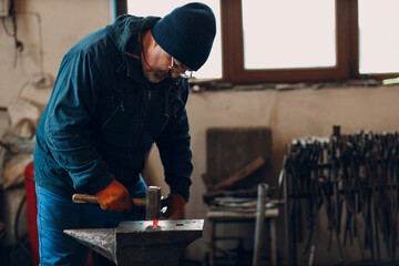 Blacksmith forges and makes metal detail with hammer and anvil at forge.