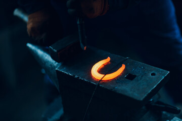 Blacksmith forges and making metal horseshoe with hammer and anvil at forge.
